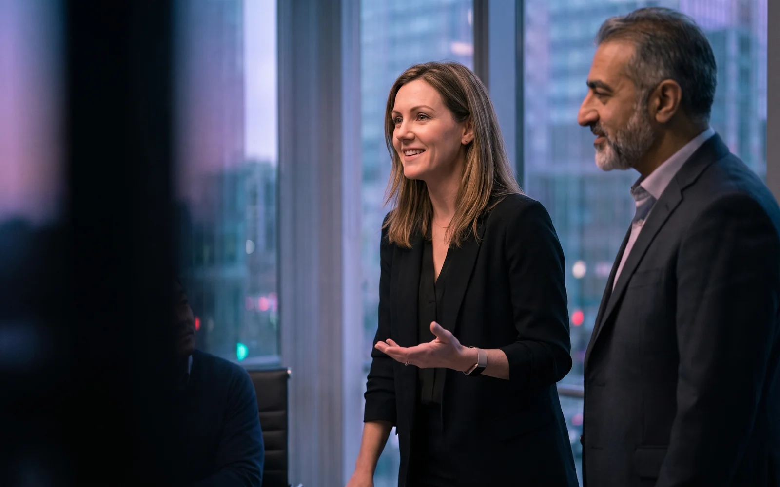 AI-generated scene: An industry expert presents with quiet confidence in an evening boardroom, her business partner beside her, smiling as he listens.